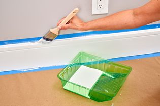 person painting trim with a paintbrush with a paint tray nearby