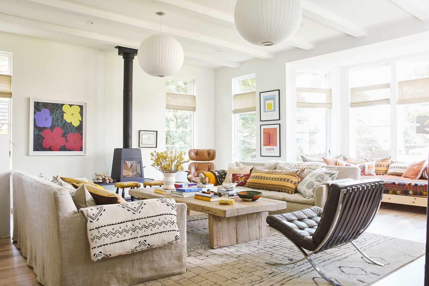 Living room with wood burning stove; large rustic coffee table, neutral colored sofas and modern leather chair with white beamed ceilings and round globular chandeliers Rating