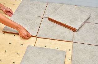 A person laying tile on plywood.