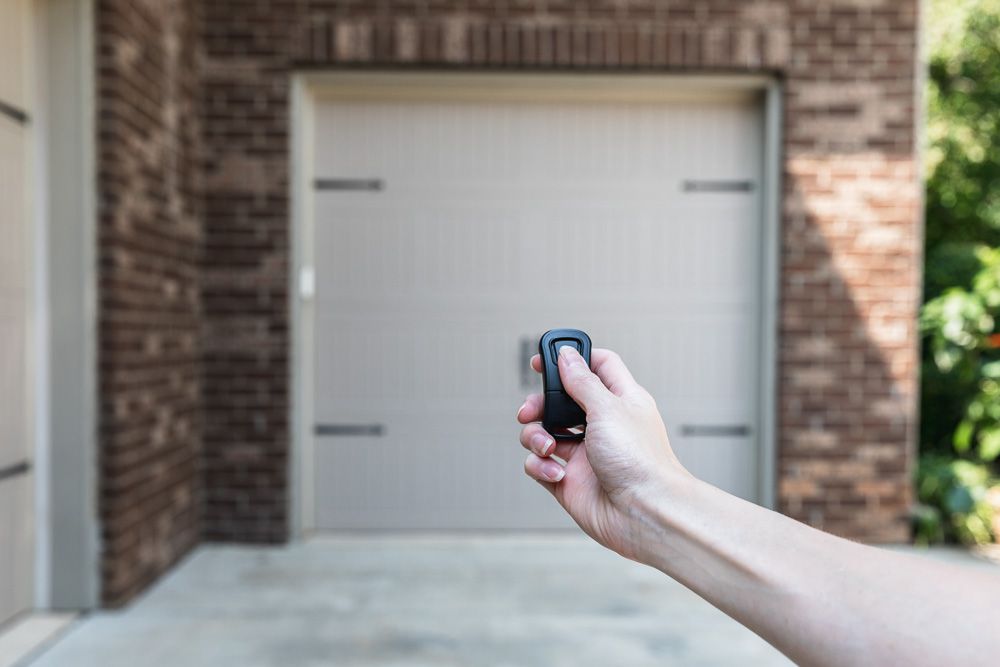 Télécommande de porte de garage en cours de pression devant une porte de garage beige