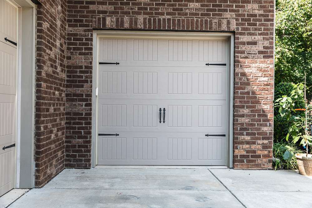 Porte de garage beige restant fermée et entourée de mur en briques