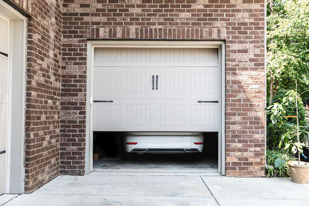 Porte de garage beige partiellement fermée avec voiture blanche à l'intérieur