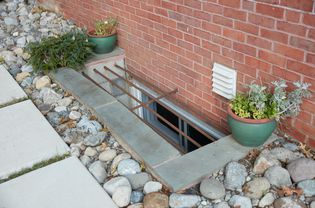 Basement window opening with bars above and surrounded by rocks and plants