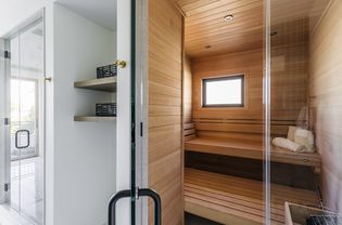 Teak-covered steam room with glass door next to white hallway