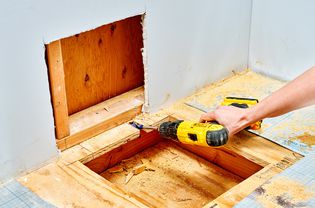 Une personne utilisant une perceuse sur un sous-plancher à côté d'un mur.