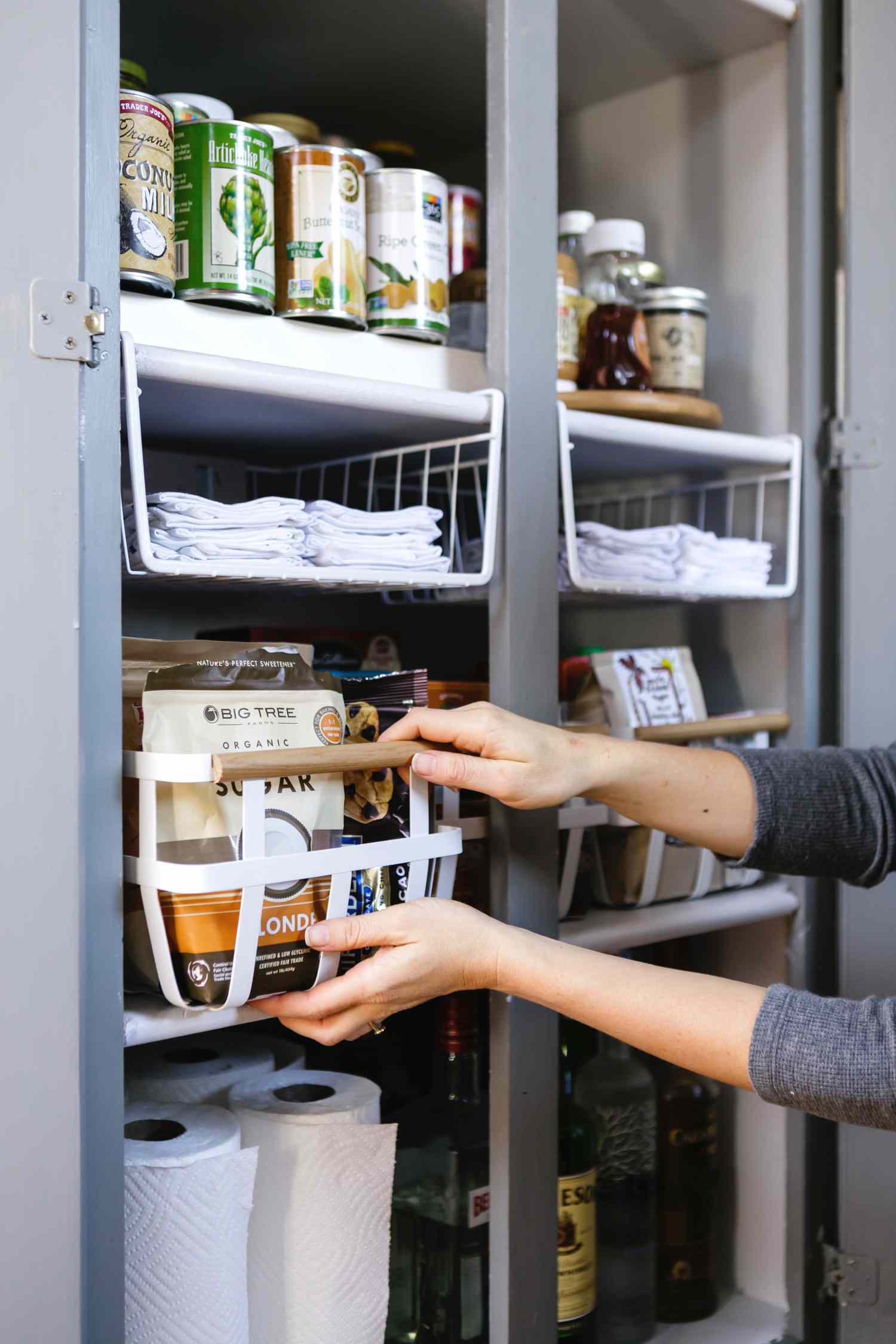 A woman pulling out a basket of food in an organized pantry.