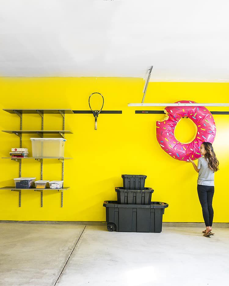 A girl hanging up an inflatable donut in a yellow garage.