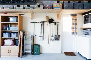 Garage organized with plastic boxes on wooden shelves and rakes held on the wall